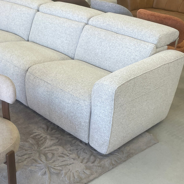 A light beige textured fabric sectional sofa with matching accent chairs, arranged on a gray patterned rug in a furniture showroom.