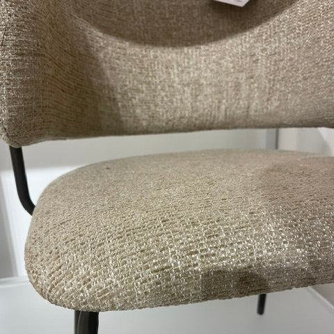 Close-up of a modern upholstered chair with a textured beige fabric seat and back, supported by slim black metal legs.