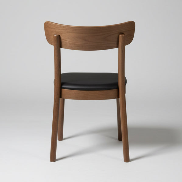 A wooden dining chair with a curved backrest and a dark seat cushion, photographed indoors against stacked cardboard boxes and a light concrete floor.