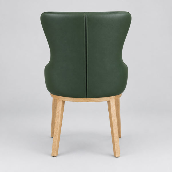 A modern wingback armchair with a dark green faux leather seat and backrest, supported by light natural wood legs, shown in a furniture showroom.