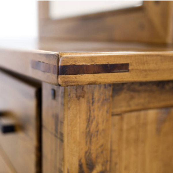 Close-up of a rustic wooden dresser with a warm honey-brown finish, dark brown inlay striping, and black drawer pulls.